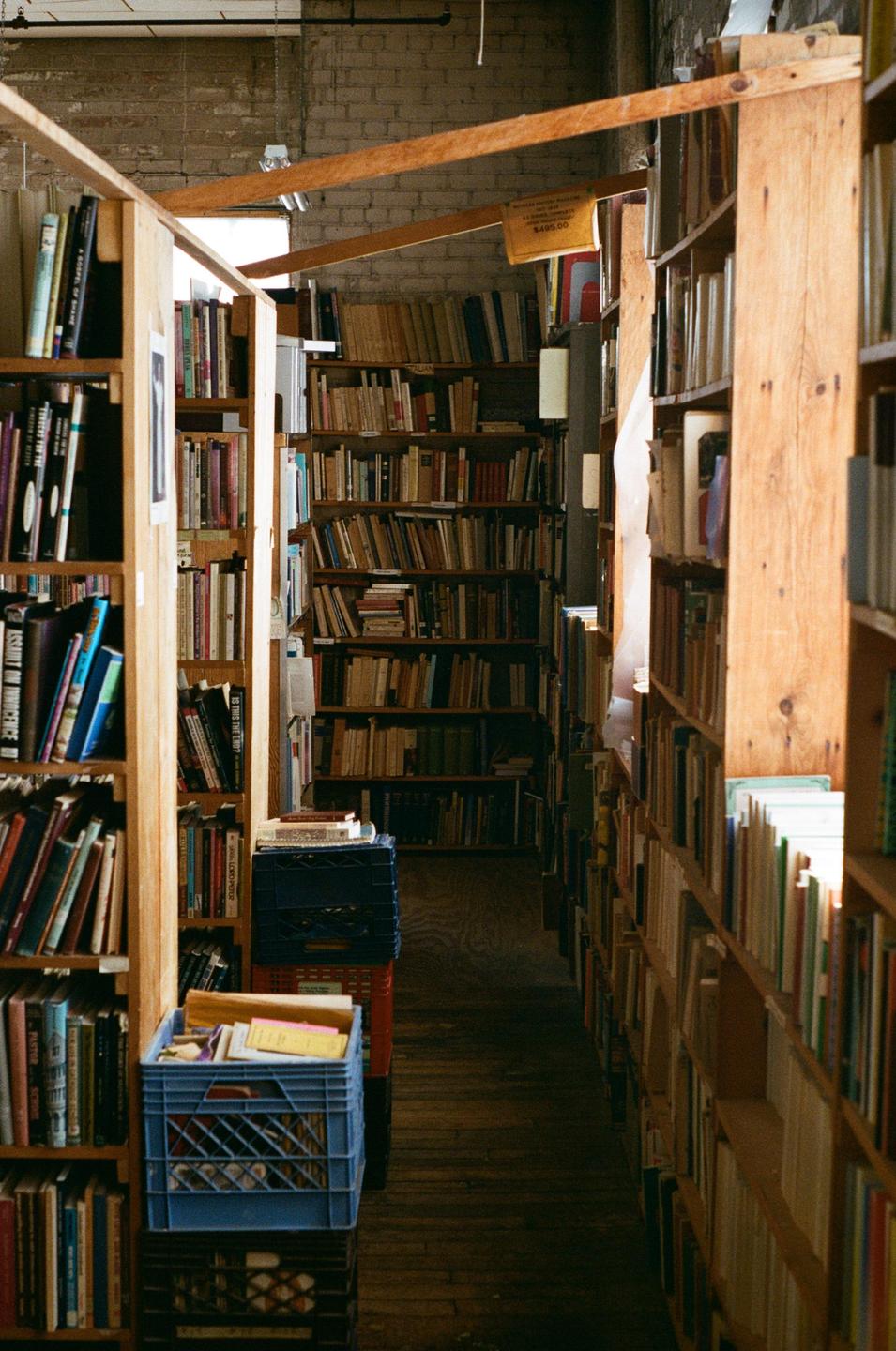 A narrow aisle in a bookstore is lined with tall wooden shelves filled with books.