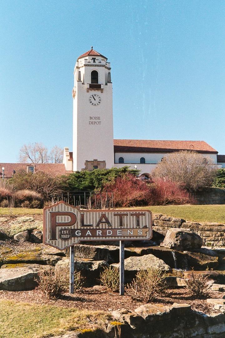 A tall clock tower with "Boise Depot" written on it stands behind a sign for Platt Gardens.