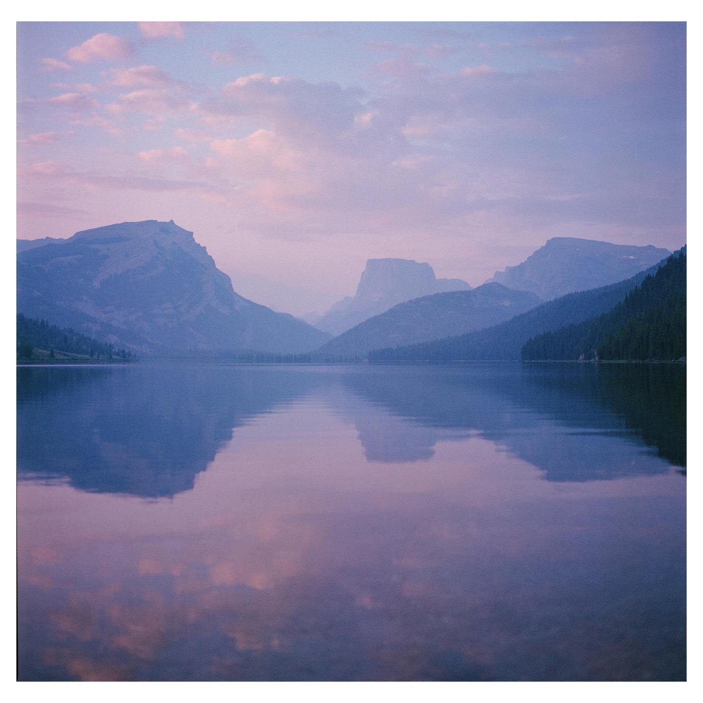 A lake reflects the purple and pink sky and mountains at sunrise.
