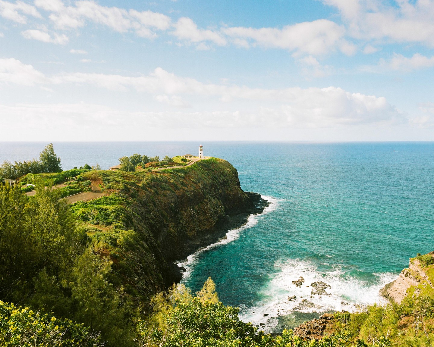 A lighthouse stands on a green cliff overlooking the Pacific Ocean.
