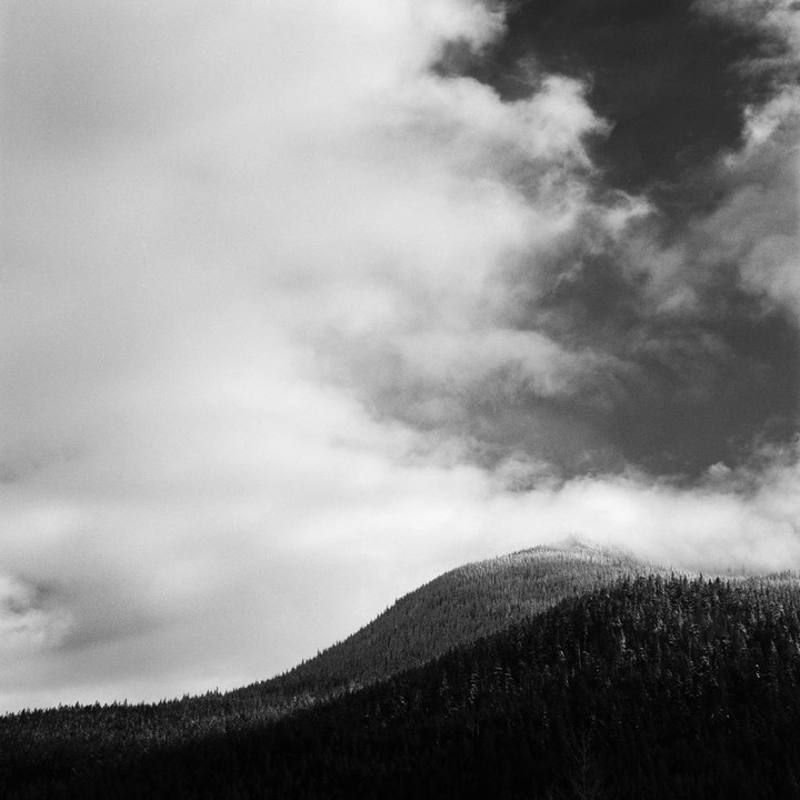 A black and white landscape shows a forested mountain under a cloudy sky.