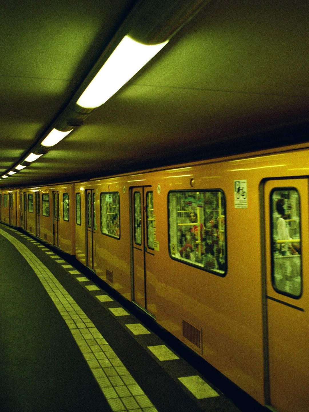 A yellow subway train is stopped at a station platform under fluorescent lights.