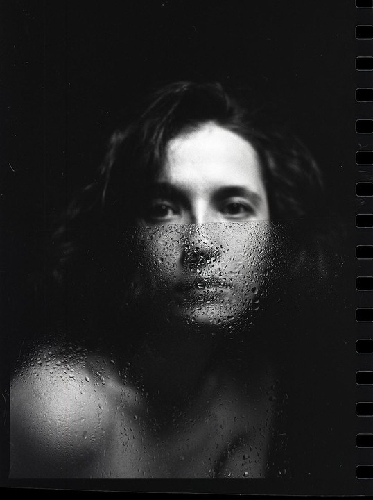 A person's face is partially obscured by a wet, textured surface with water droplets, creating a split image.