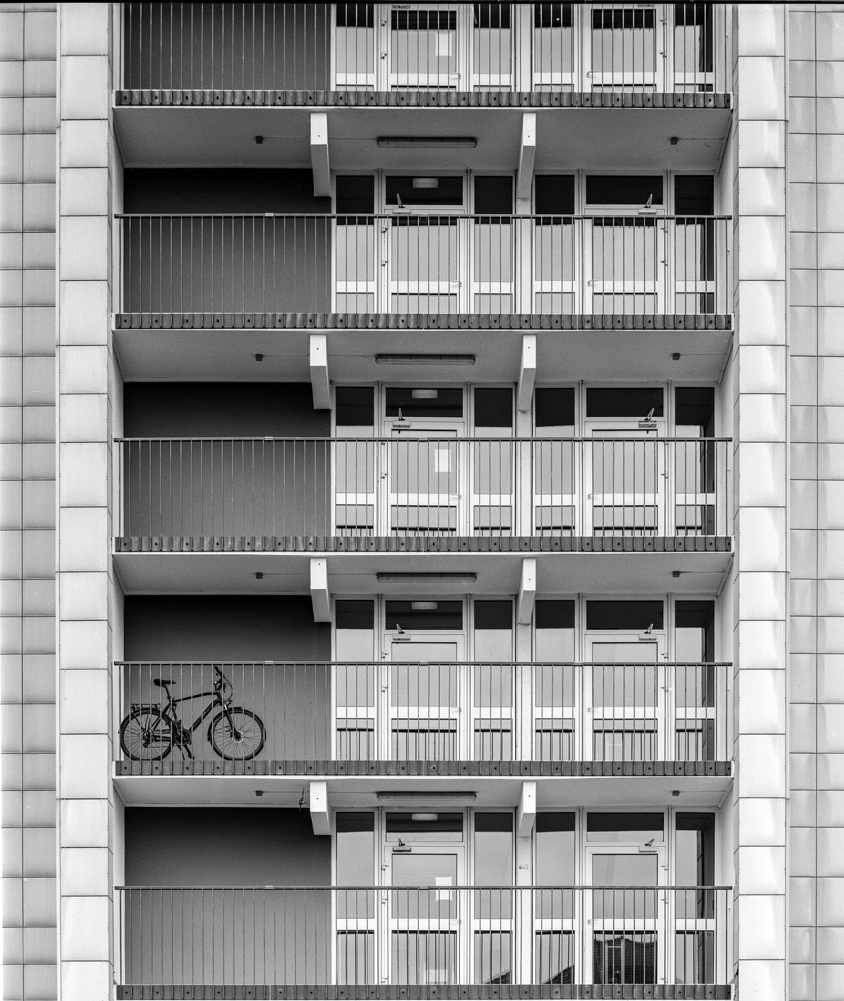 A bicycle is parked on a balcony of a multi-story building with many identical balconies and windows.