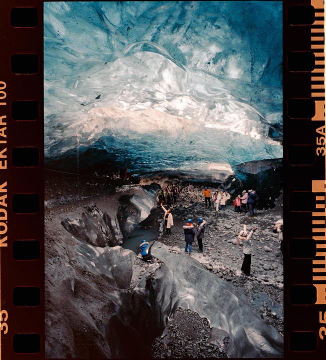 A group of people stand inside a large ice cave with blue and white ice formations.
