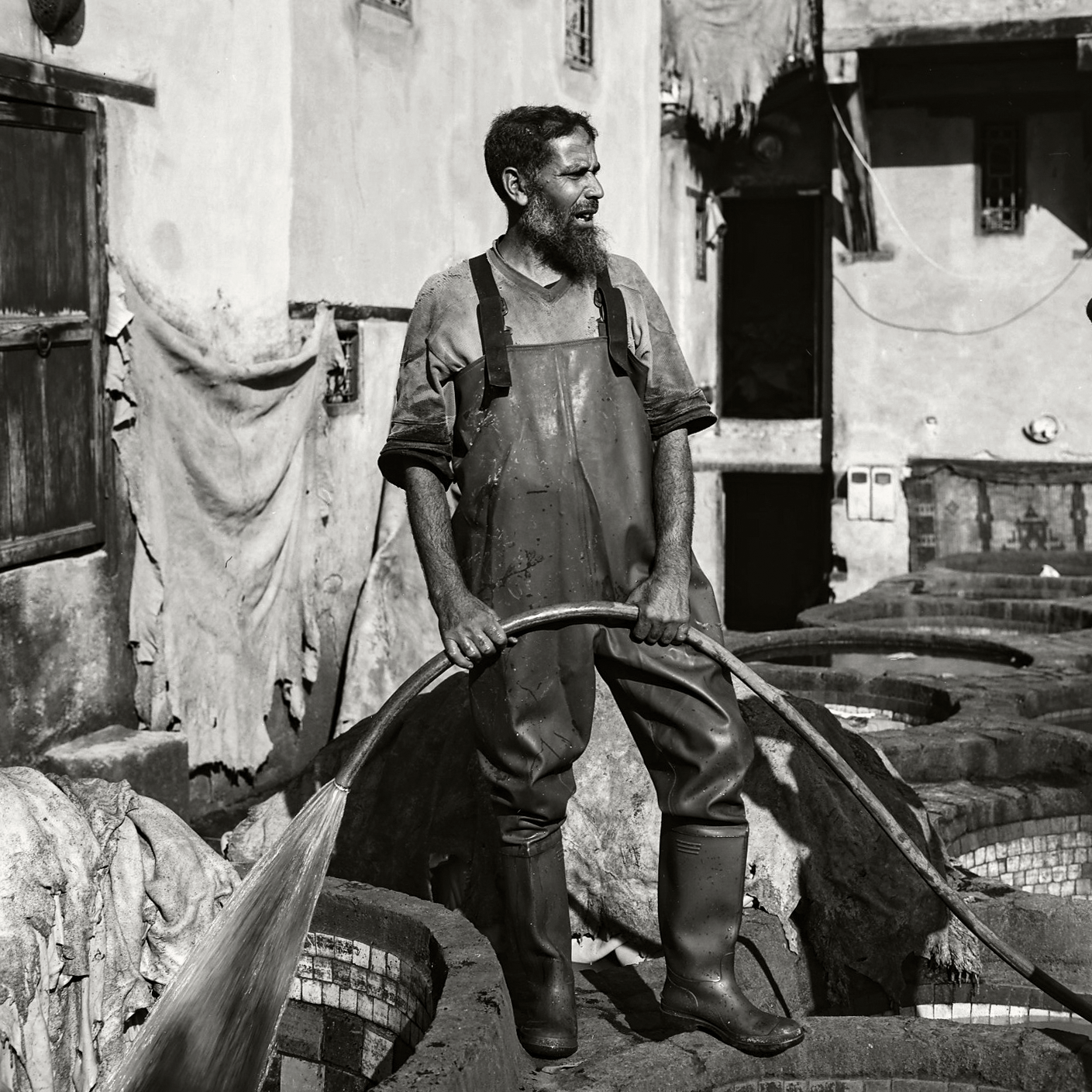 A man in waders and boots holds a hose, spraying water into a vat at a tannery.