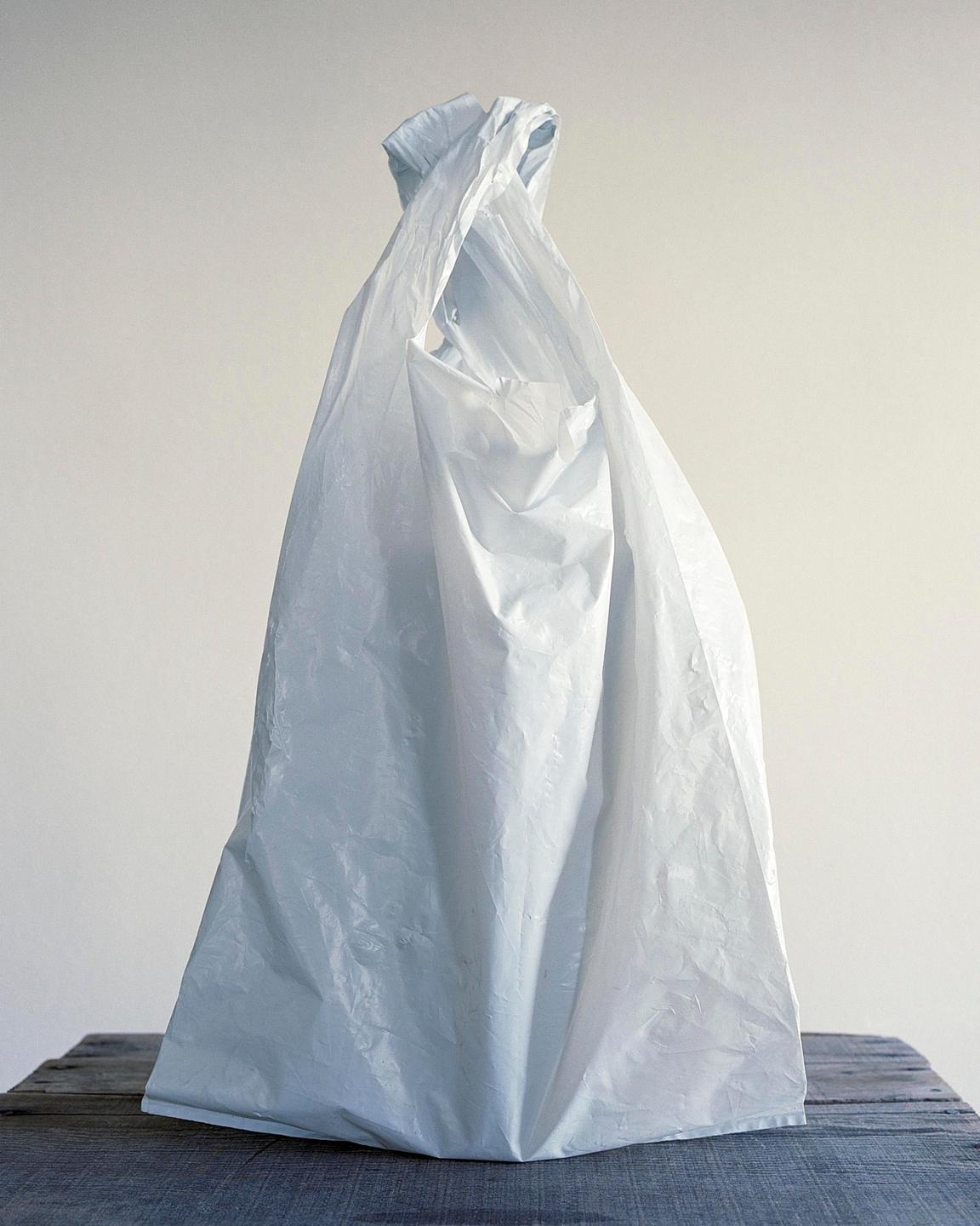 A white plastic bag sits on a wooden surface against a light background.