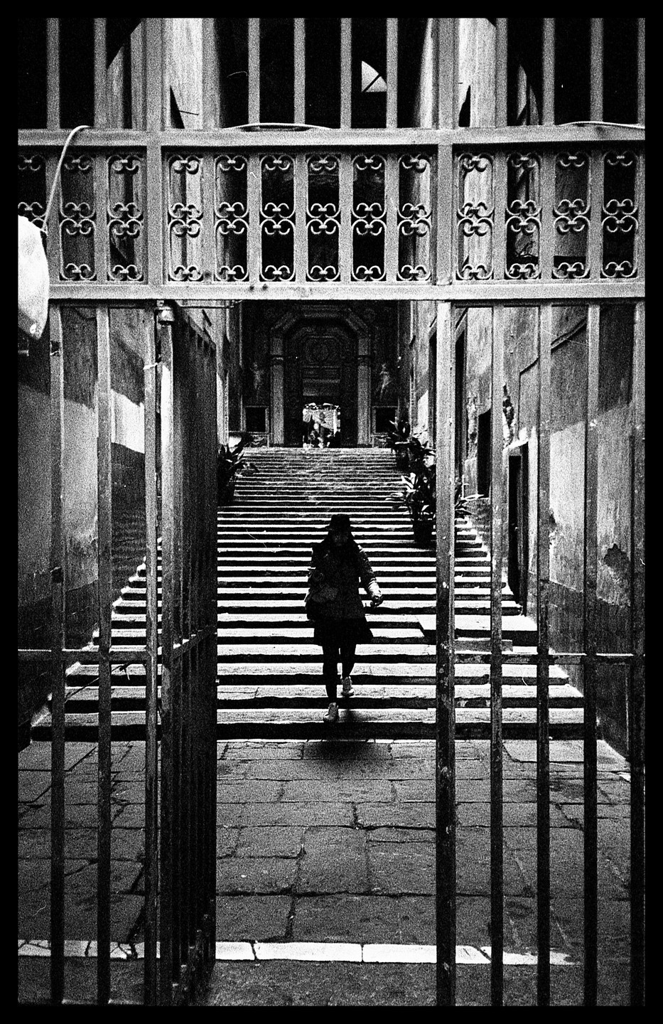 A woman walks up a long, wide staircase through an open ornate metal gate.