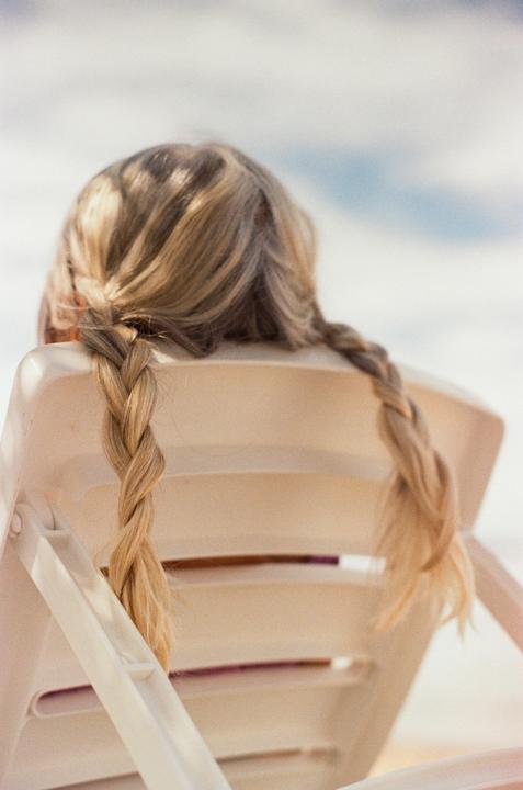 A woman with blonde braided hair sits in a white chair with her back to the viewer.