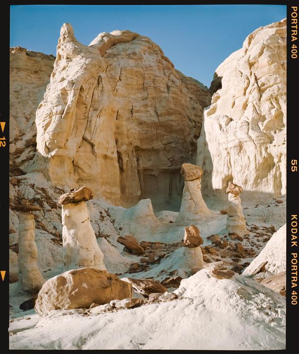 A desert landscape features light-colored rock formations and hoodoos under a clear blue sky.