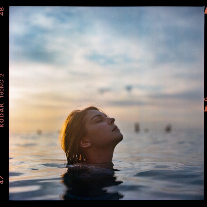 A woman with her head tilted back is in the water with the sky in the background.