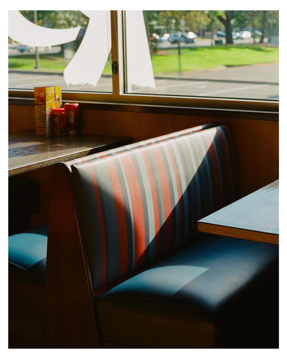Sunlight casts a shadow across a striped booth in a diner.