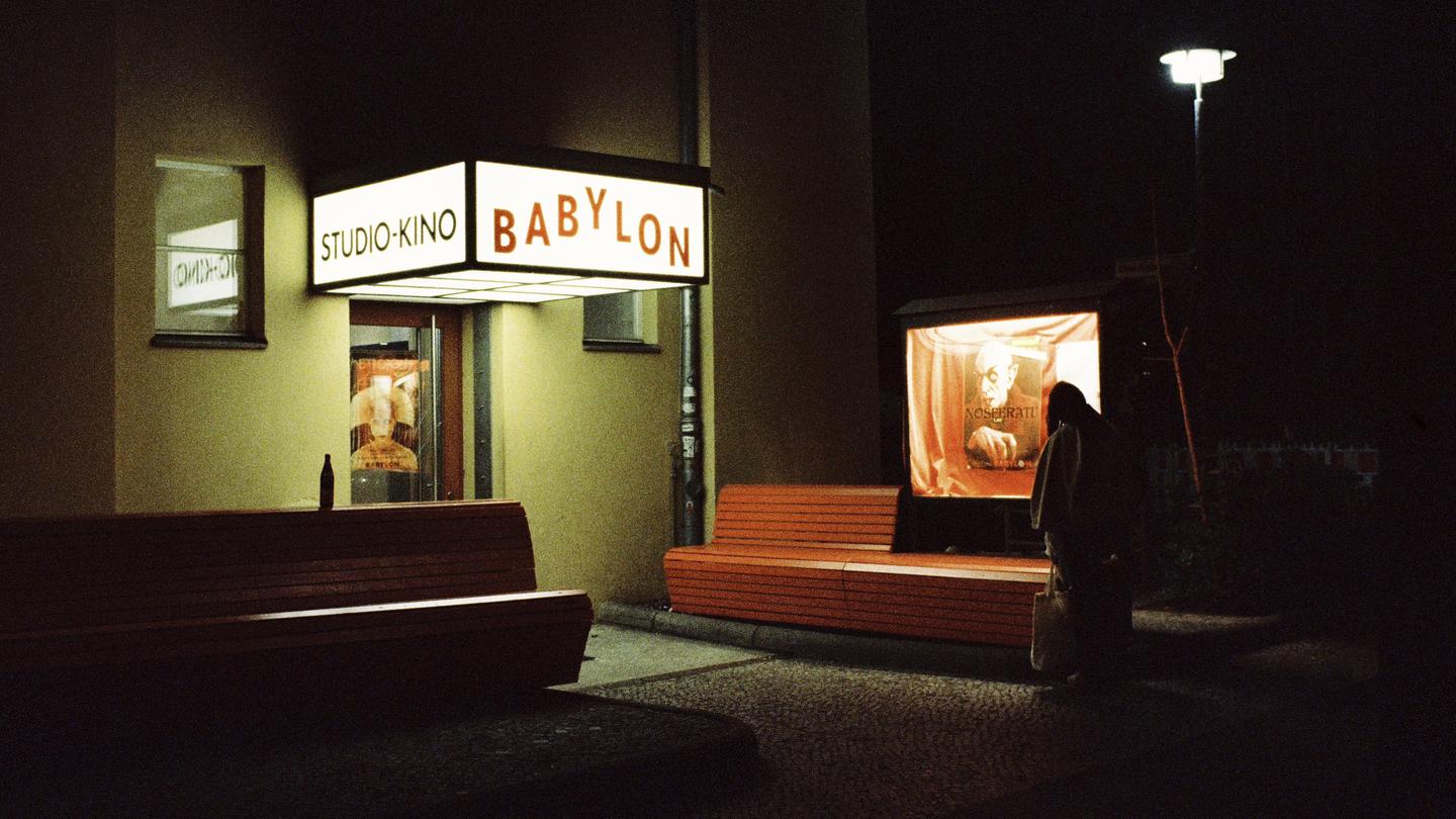 A person stands in front of a movie theater at night with a poster for Nosferatu visible.