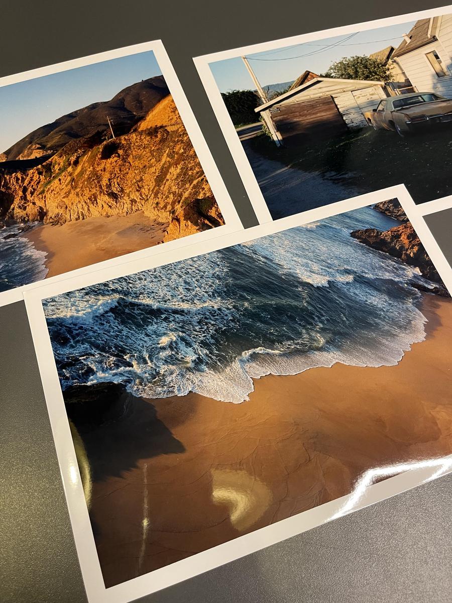 Three photographic prints are displayed on a dark surface, with the largest print showing a sandy beach with waves.