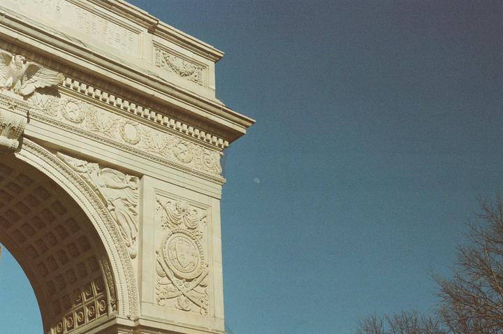 A detailed section of a stone archway with carvings is visible against a clear blue sky with a faint moon.