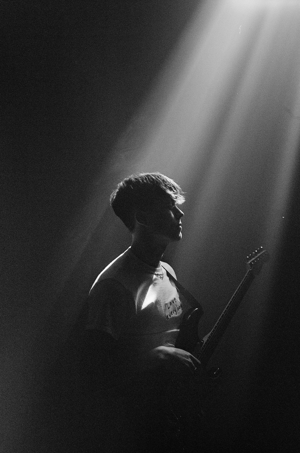 A man with a guitar is illuminated by a spotlight from above.