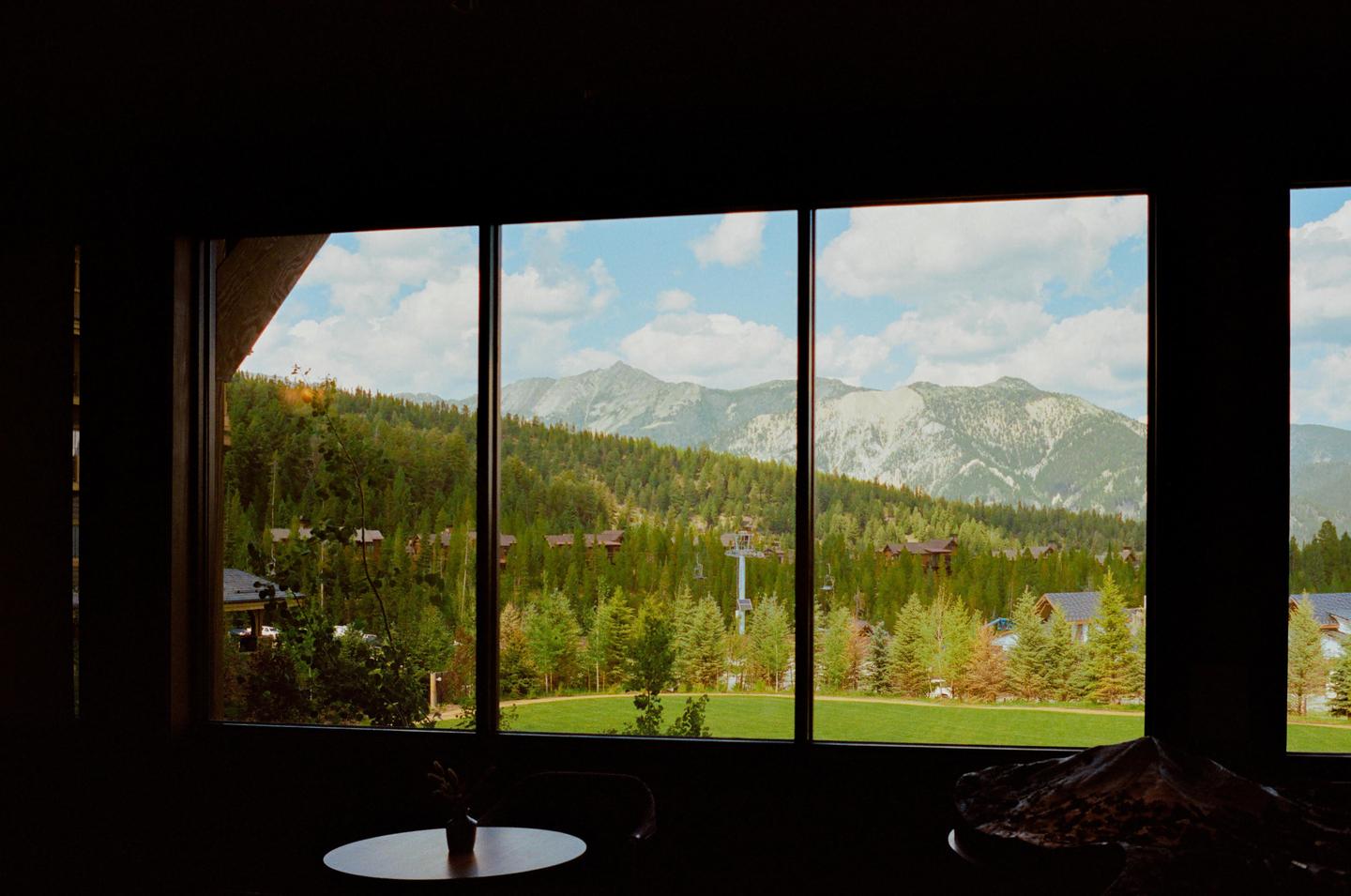 A large window looks out onto a mountain landscape with a forest, houses, and a ski lift.