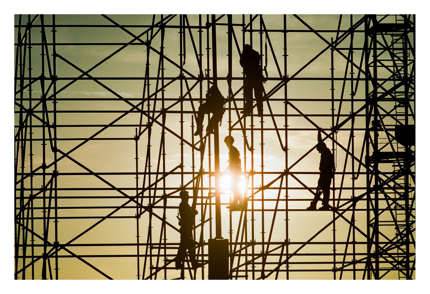 Silhouetted construction workers are visible on scaffolding against a bright sky.