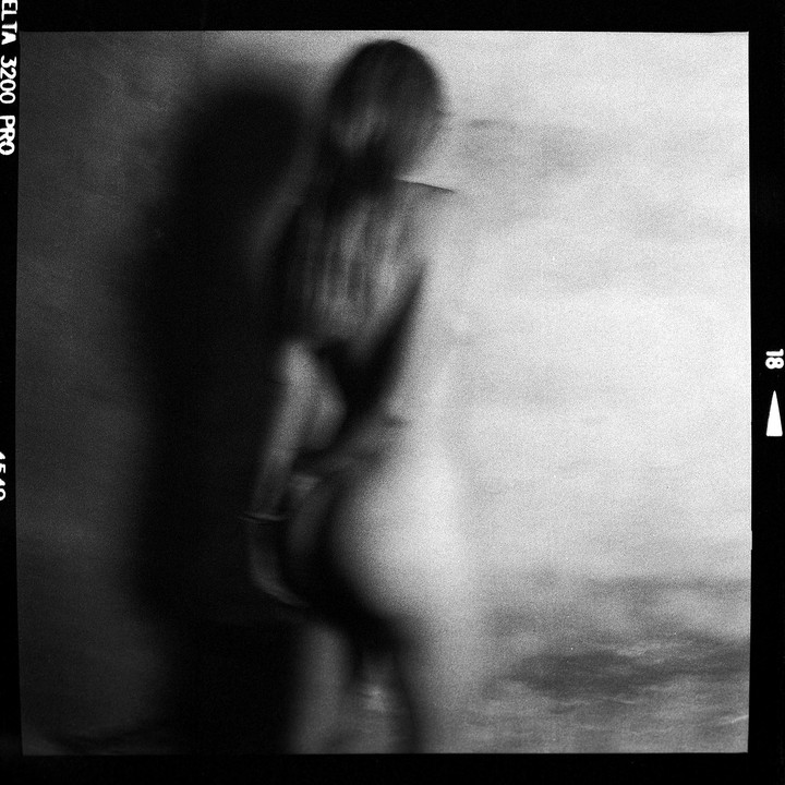 A blurry figure of a woman stands with her back to the viewer, casting a shadow on a wall.