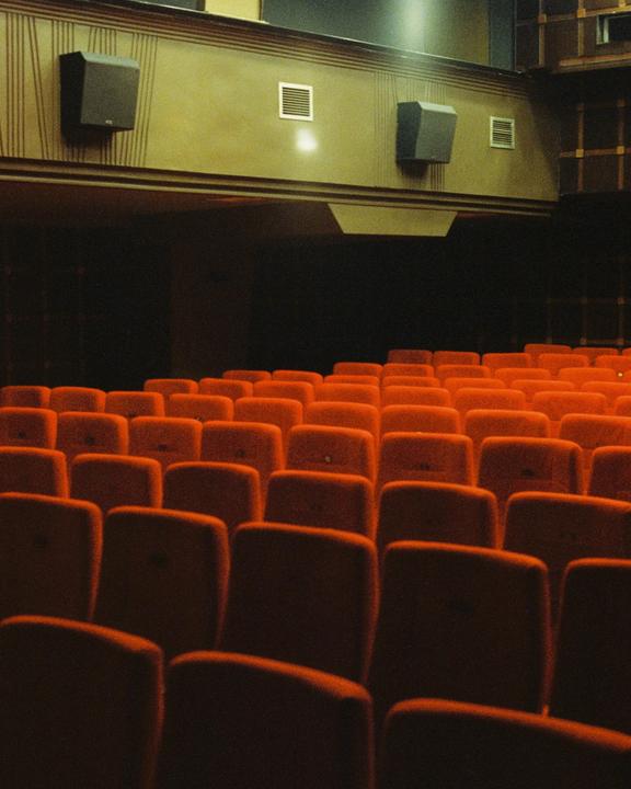 Rows of empty red seats fill a dark movie theater.