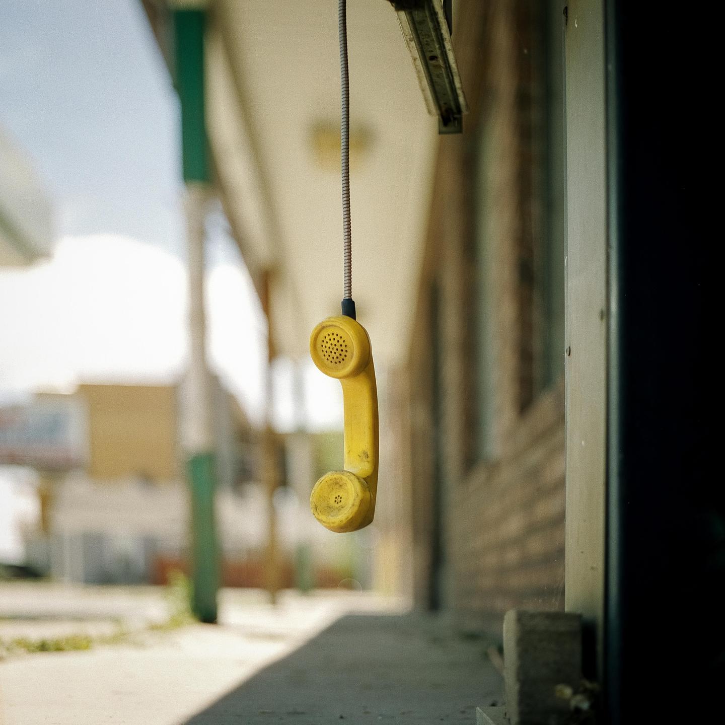 A yellow telephone receiver hangs from a coiled cord under an awning next to a brick building.