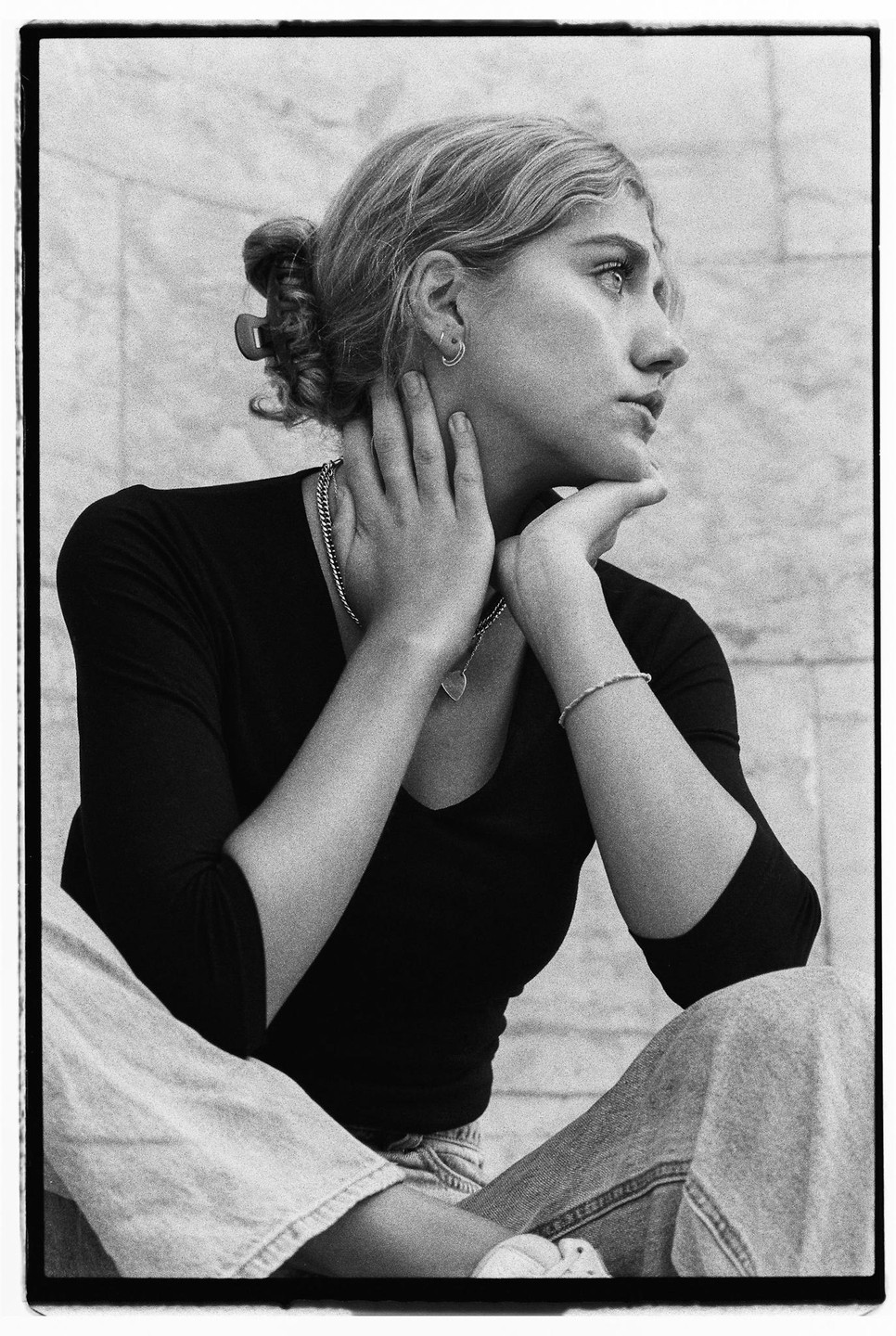 A woman with her hair in a bun sits with her hands on her neck and chin, looking to the right.