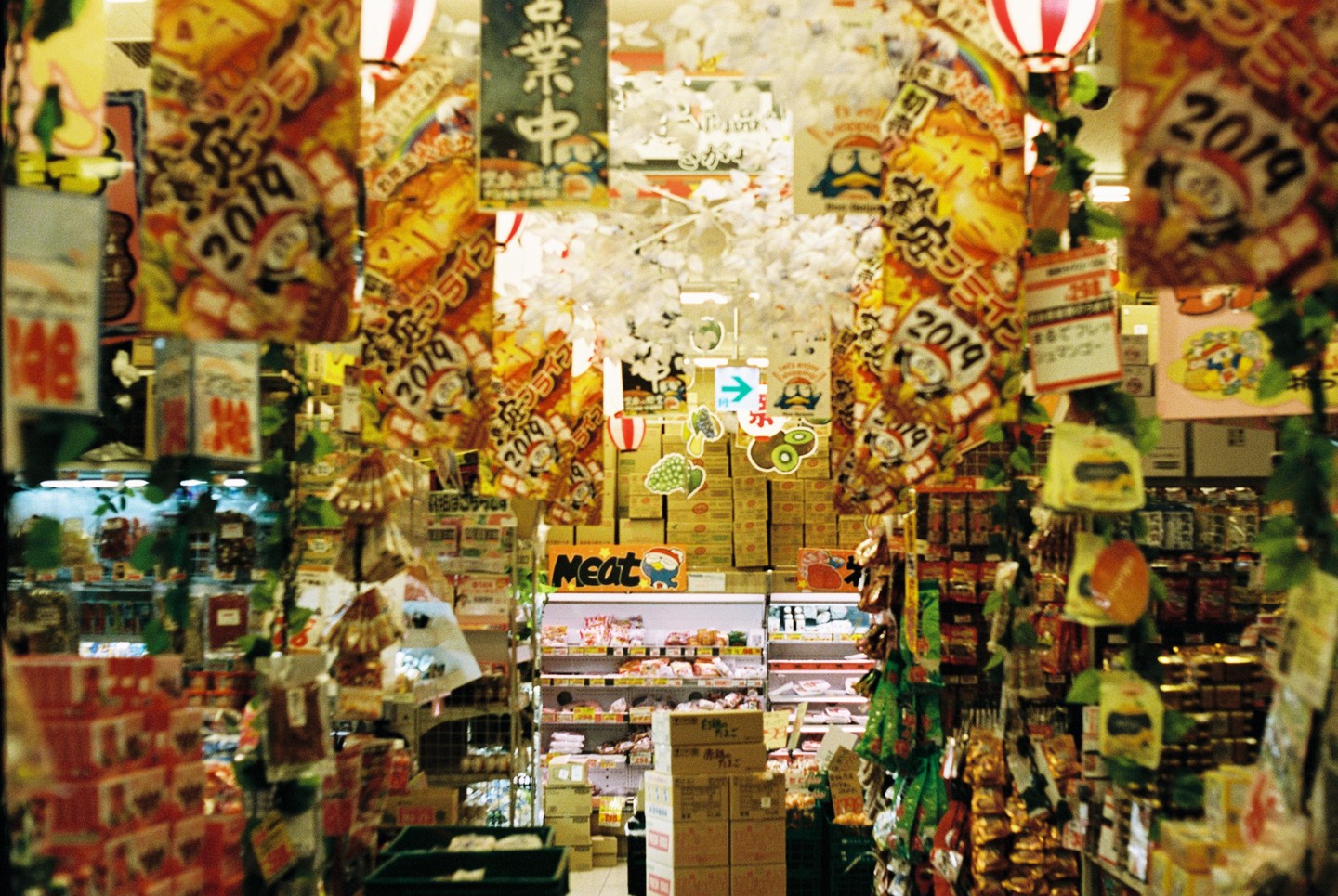 Aisle in a Japanese supermarket with many colorful signs and decorations hanging from the ceiling.