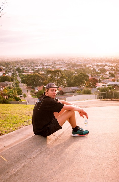 A man sits on a curb overlooking a city at sunset.