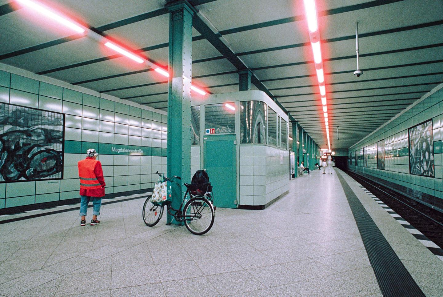 A person in a red jacket stands on a subway platform next to a bicycle.