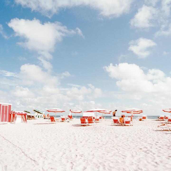 A wide shot shows a beach with red and white striped umbrellas and lounge chairs, with a few people relaxing under the sun.