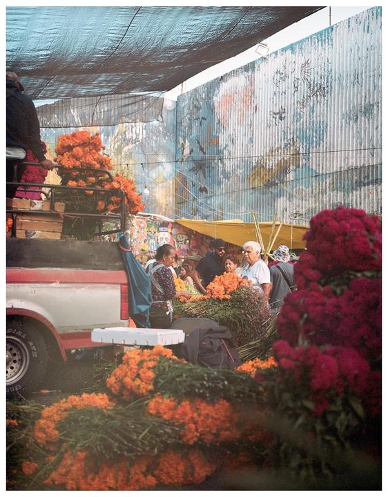 People are gathered around a truck filled with orange and red flowers at a market.