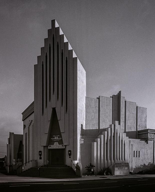 A large, angular church building with a prominent steeple stands beside a street.