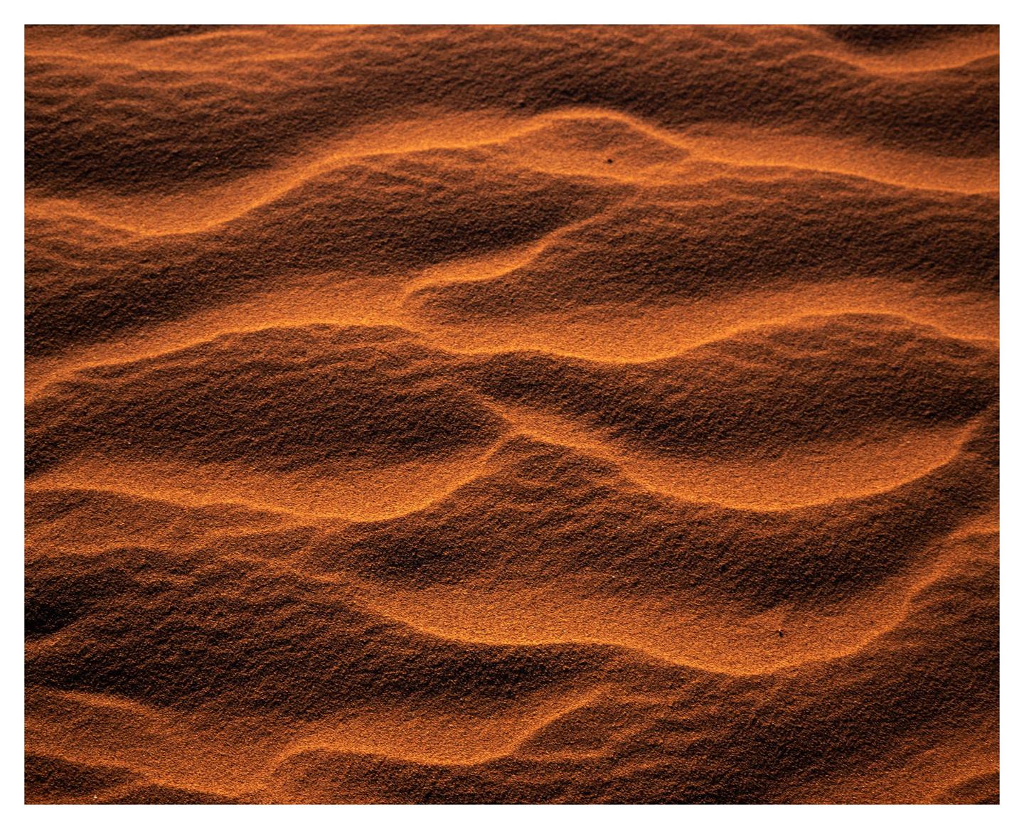 The image shows a close-up of sand dunes with ripples and shadows.