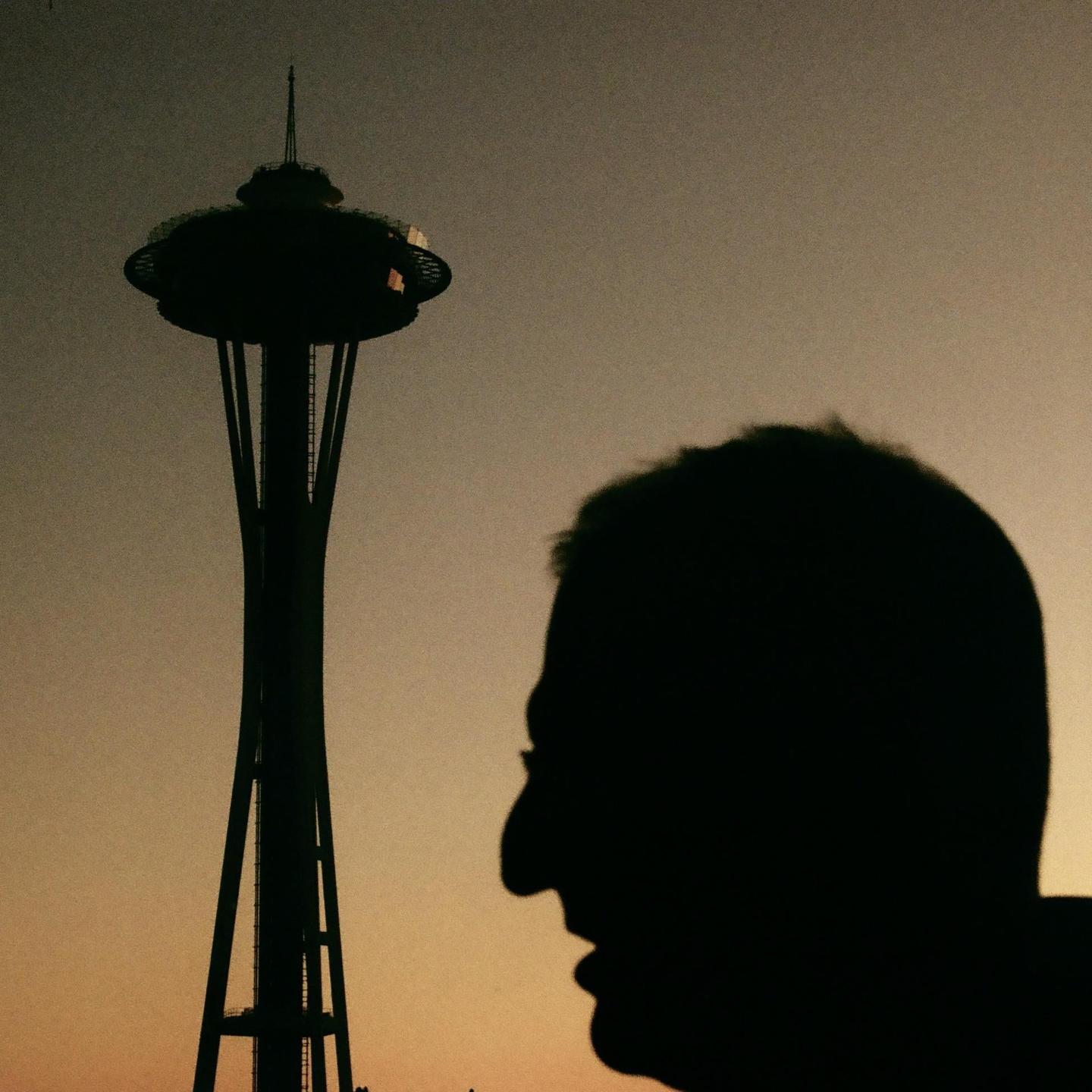 A man's silhouette is visible in the foreground with the Space Needle in the background.