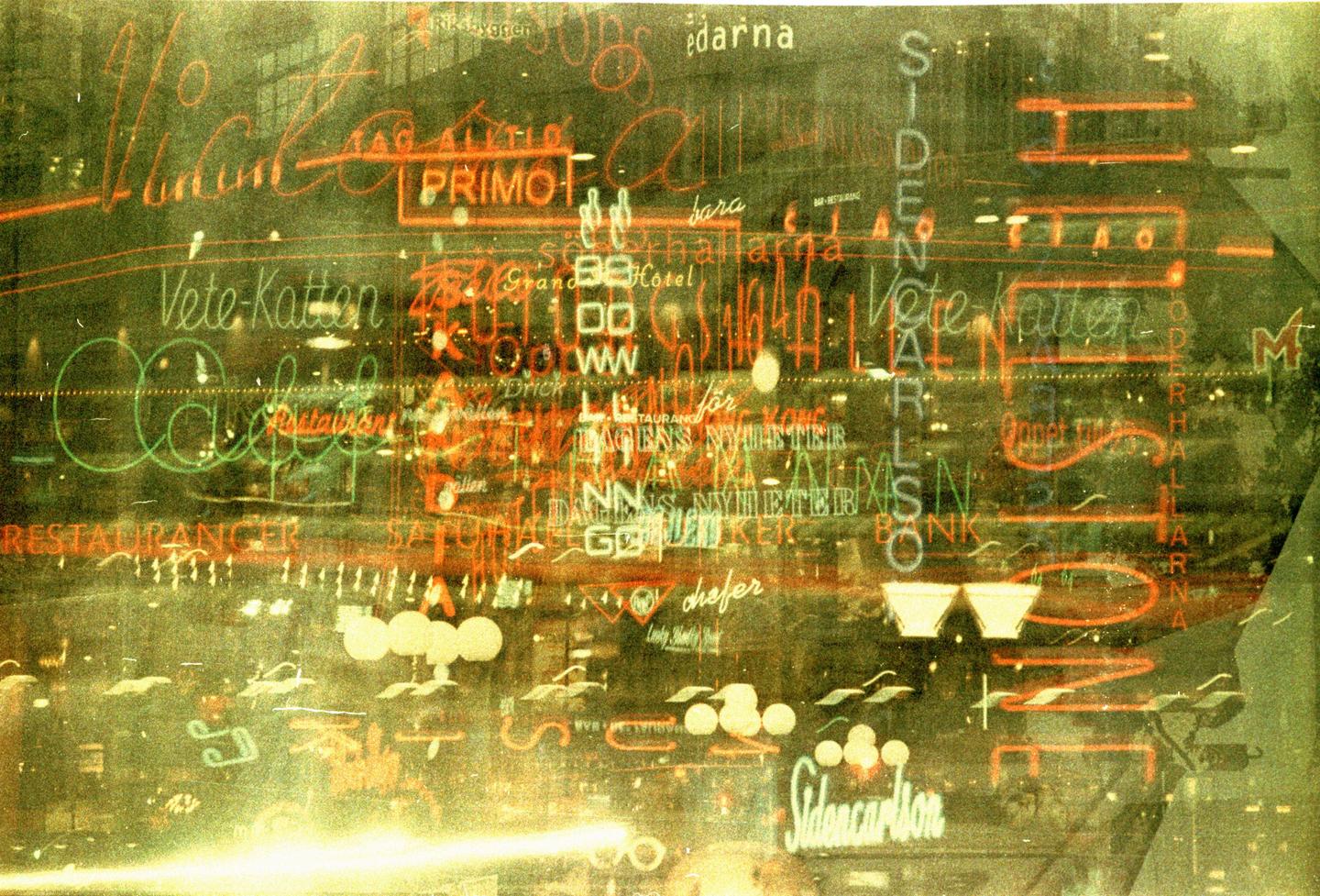 Multiple exposures of neon signs create an abstract pattern of light and text.