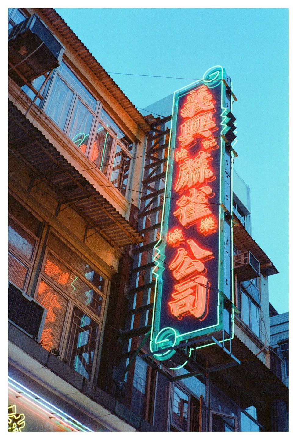 A tall neon sign with Chinese characters in red and green stands vertically on the side of a building.