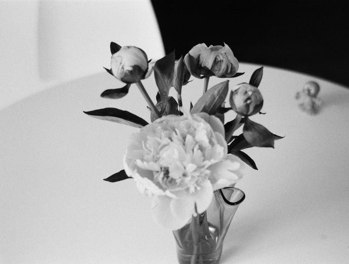 A bouquet of peonies in a vase sits on a table.