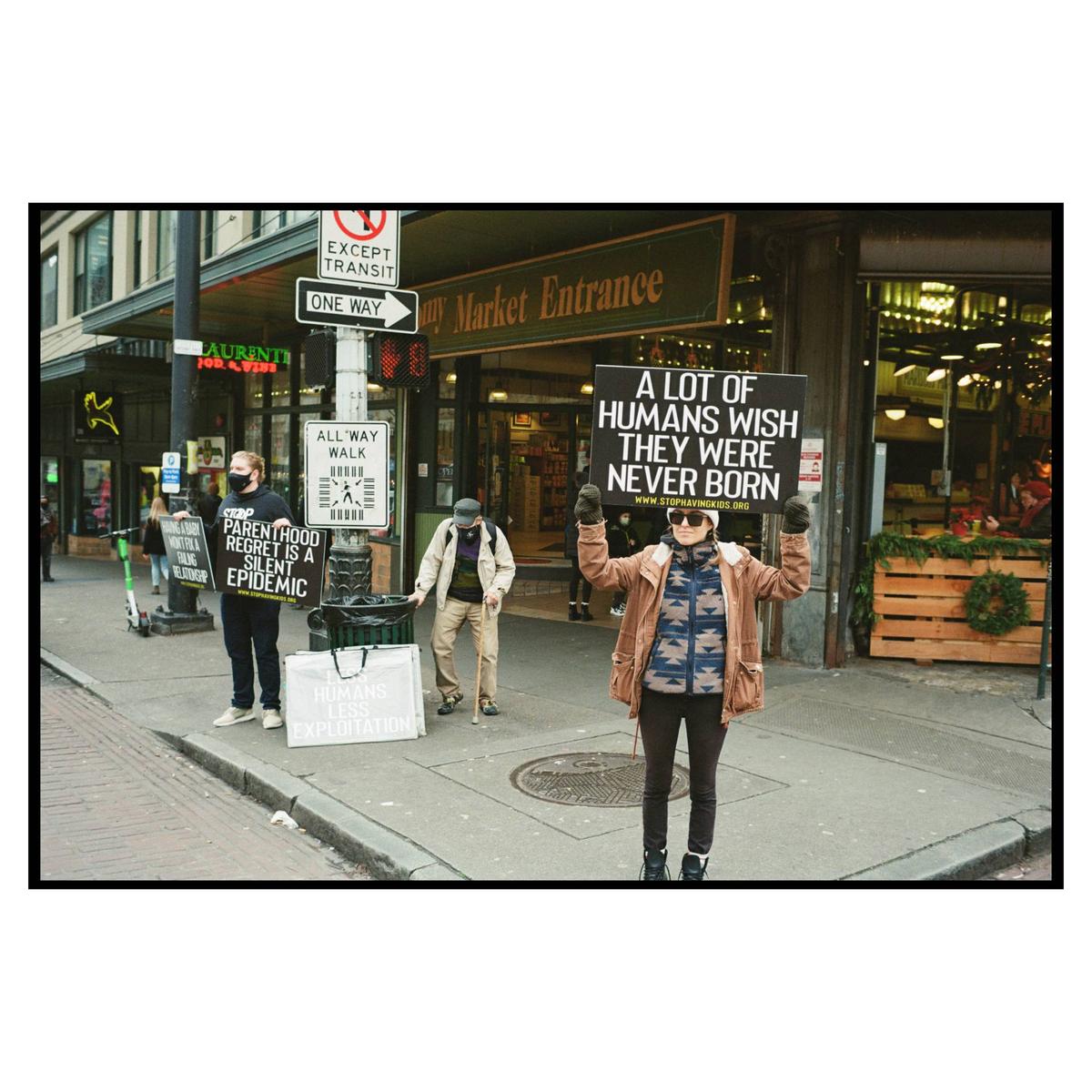 A woman holds a sign that reads "A lot of humans wish they were never born" on a city street.