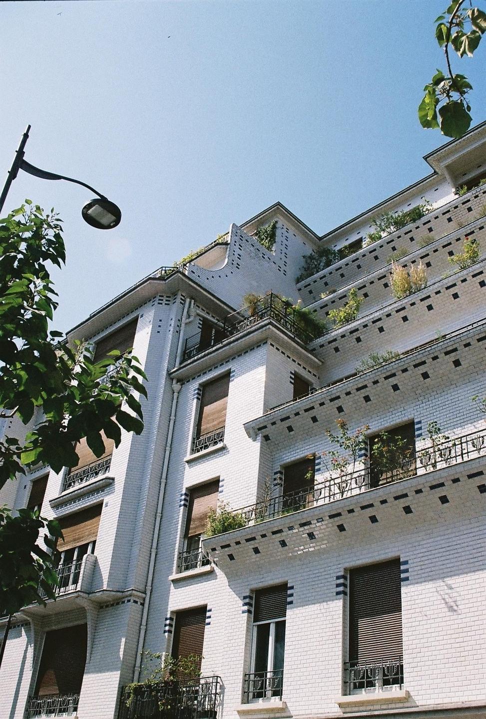 A white brick building with many balconies and plants is viewed from below.