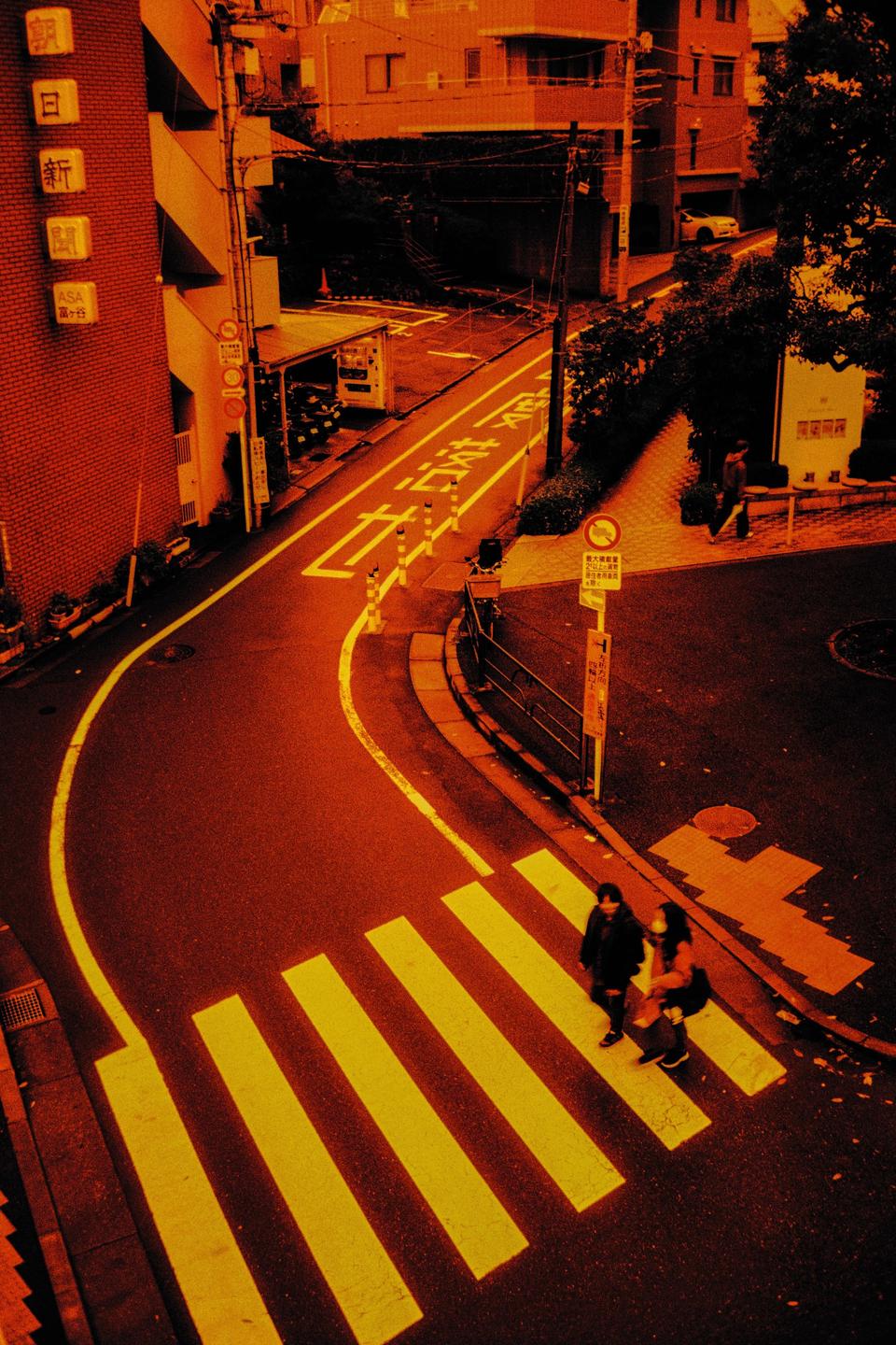 Two people walk across a crosswalk on a street in a city.