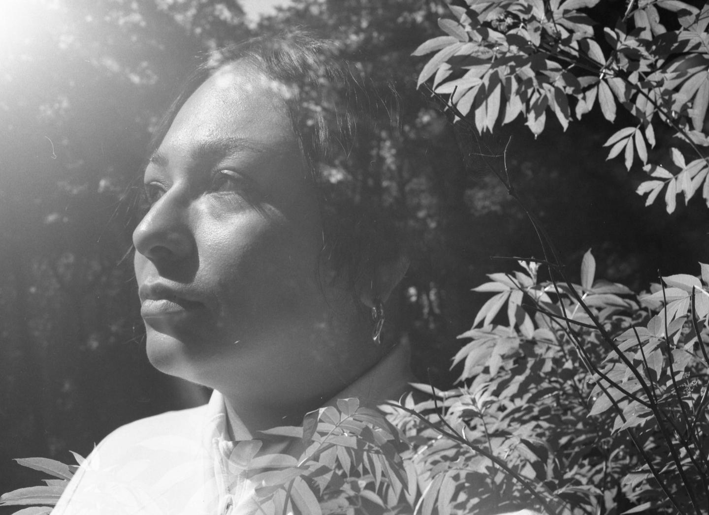 A woman is looking up with sunlight on her face, surrounded by foliage.