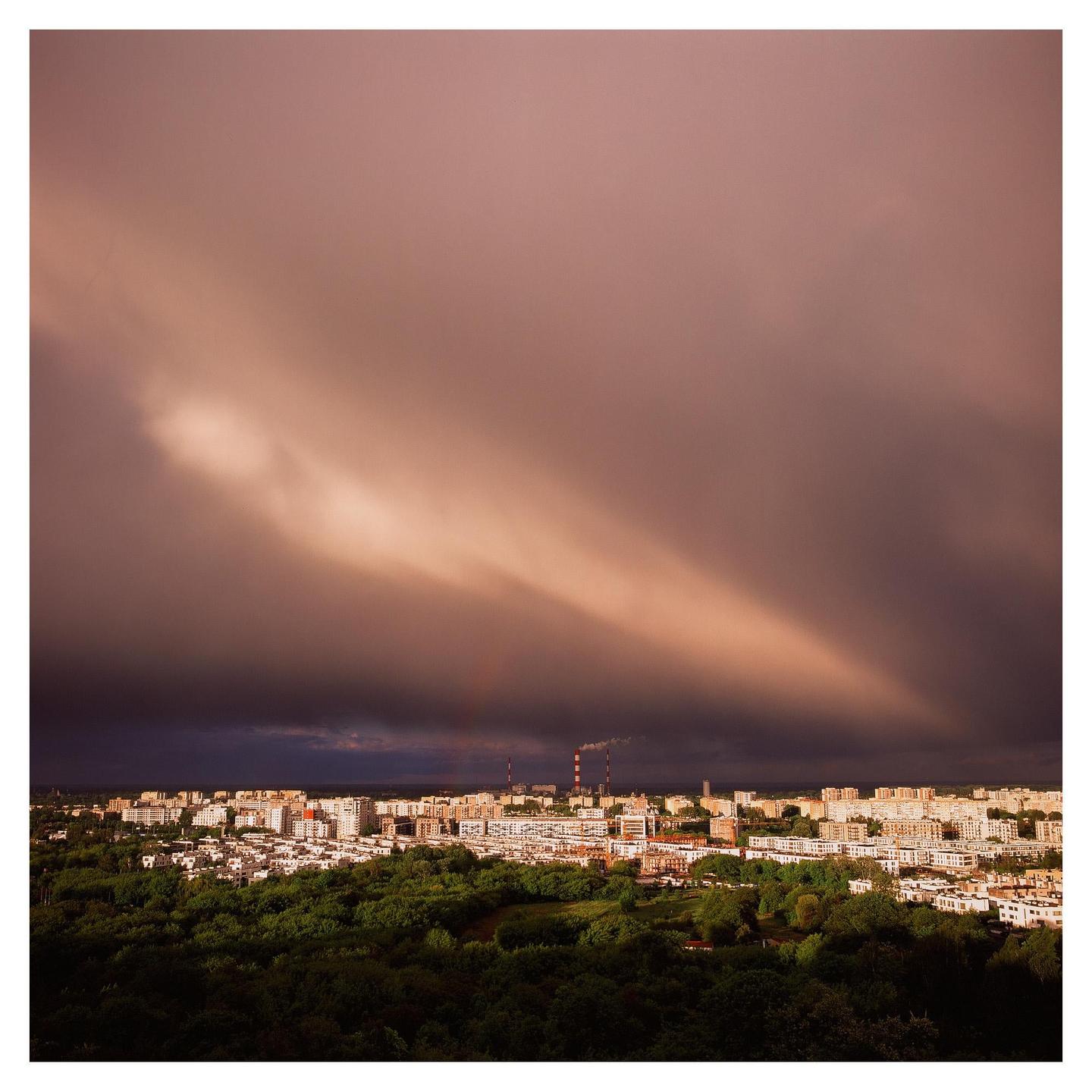 A dramatic sky with a shaft of light illuminates a city with many buildings and green trees.
