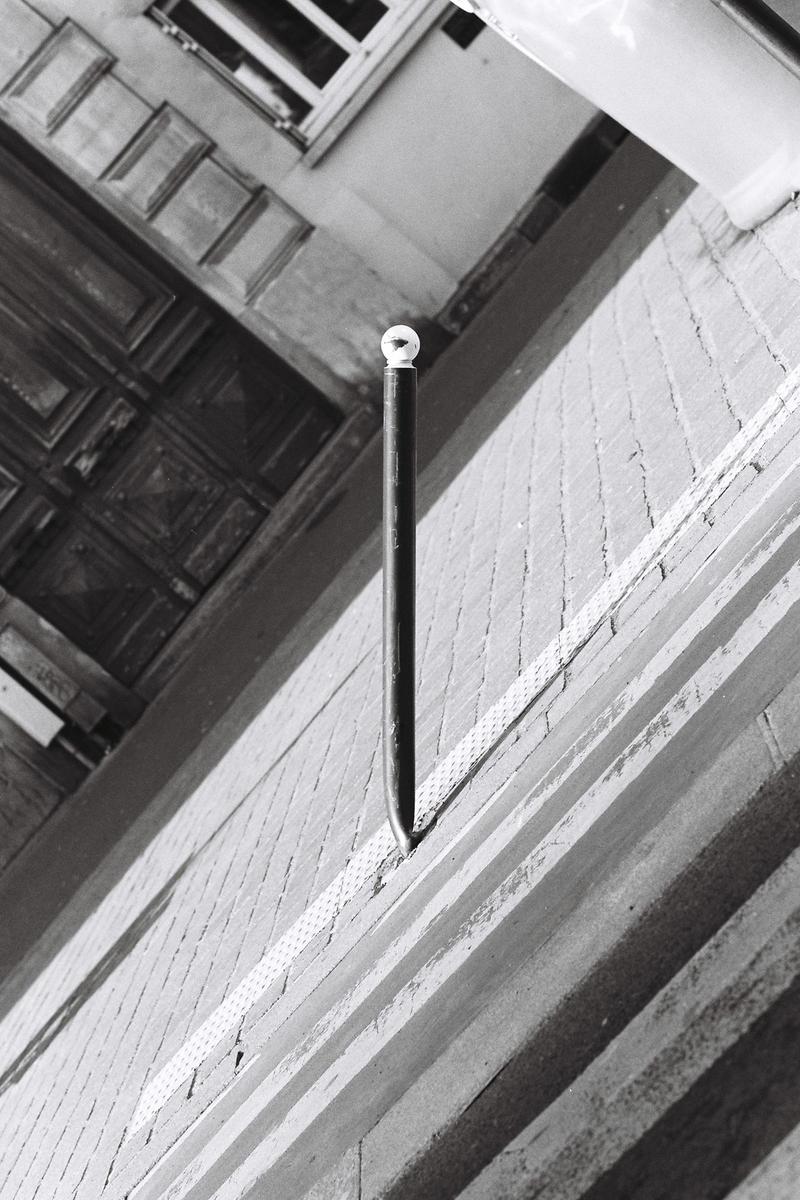 A black pole with a white spherical top is planted in a brick wall, casting a shadow.