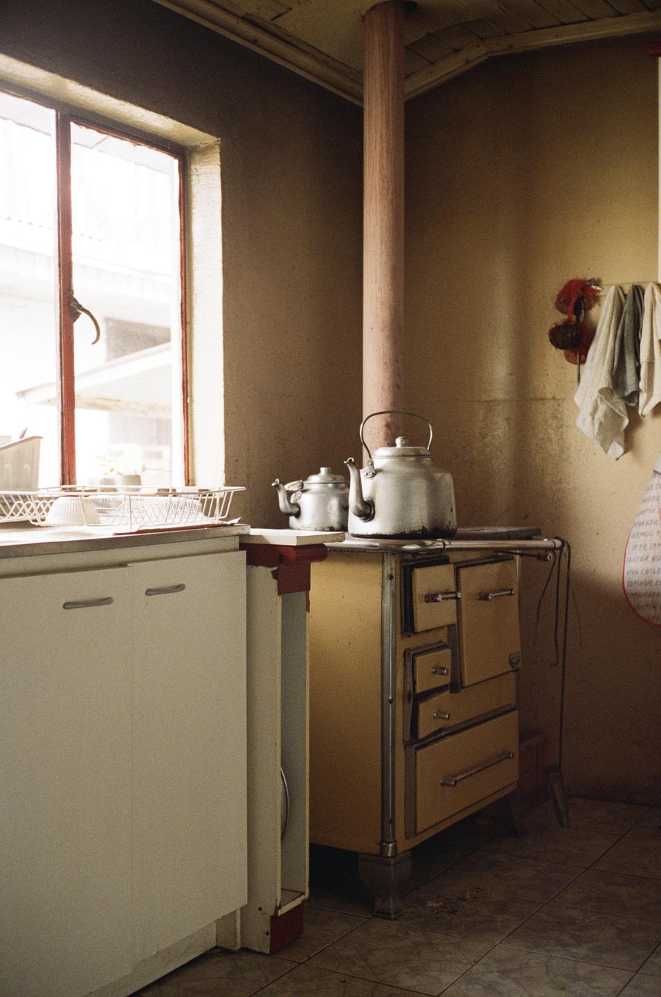 Two kettles sit on a yellow stove next to a window in a kitchen.