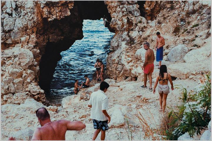 A group of people are on a rocky beach with a natural archway leading to the sea.