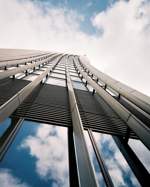 A modern building with a curved facade and many windows reflects the sky.
