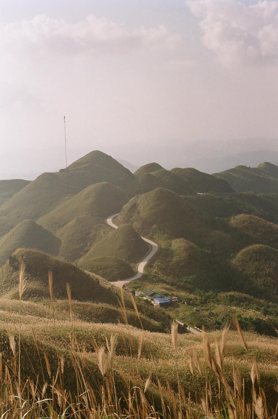 A winding road cuts through rolling green hills under a hazy sky.