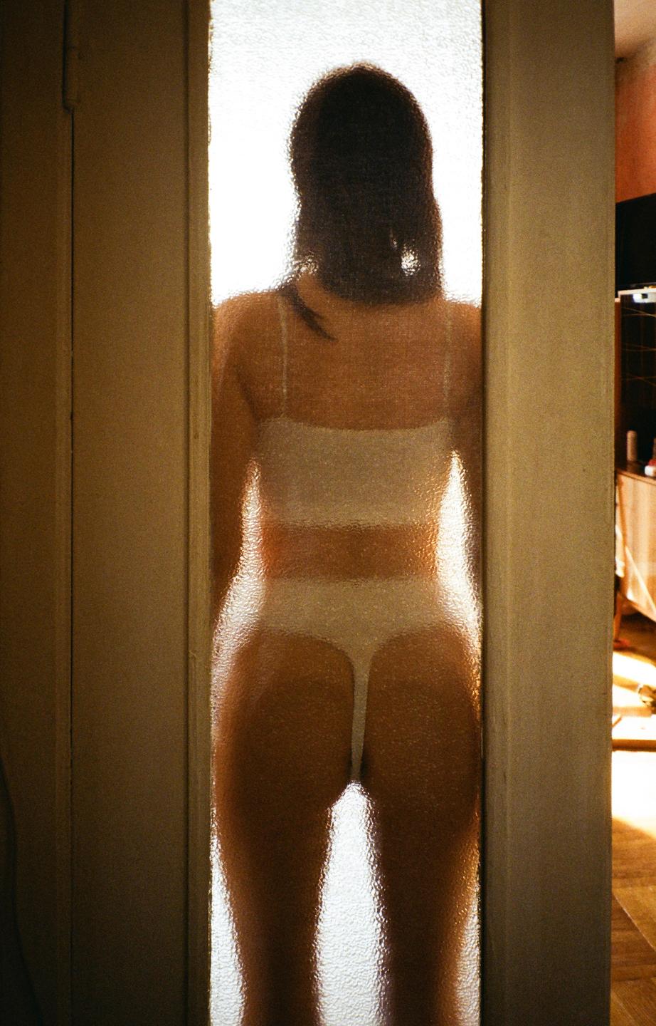 A woman stands behind a translucent door, her silhouette visible through the textured glass.