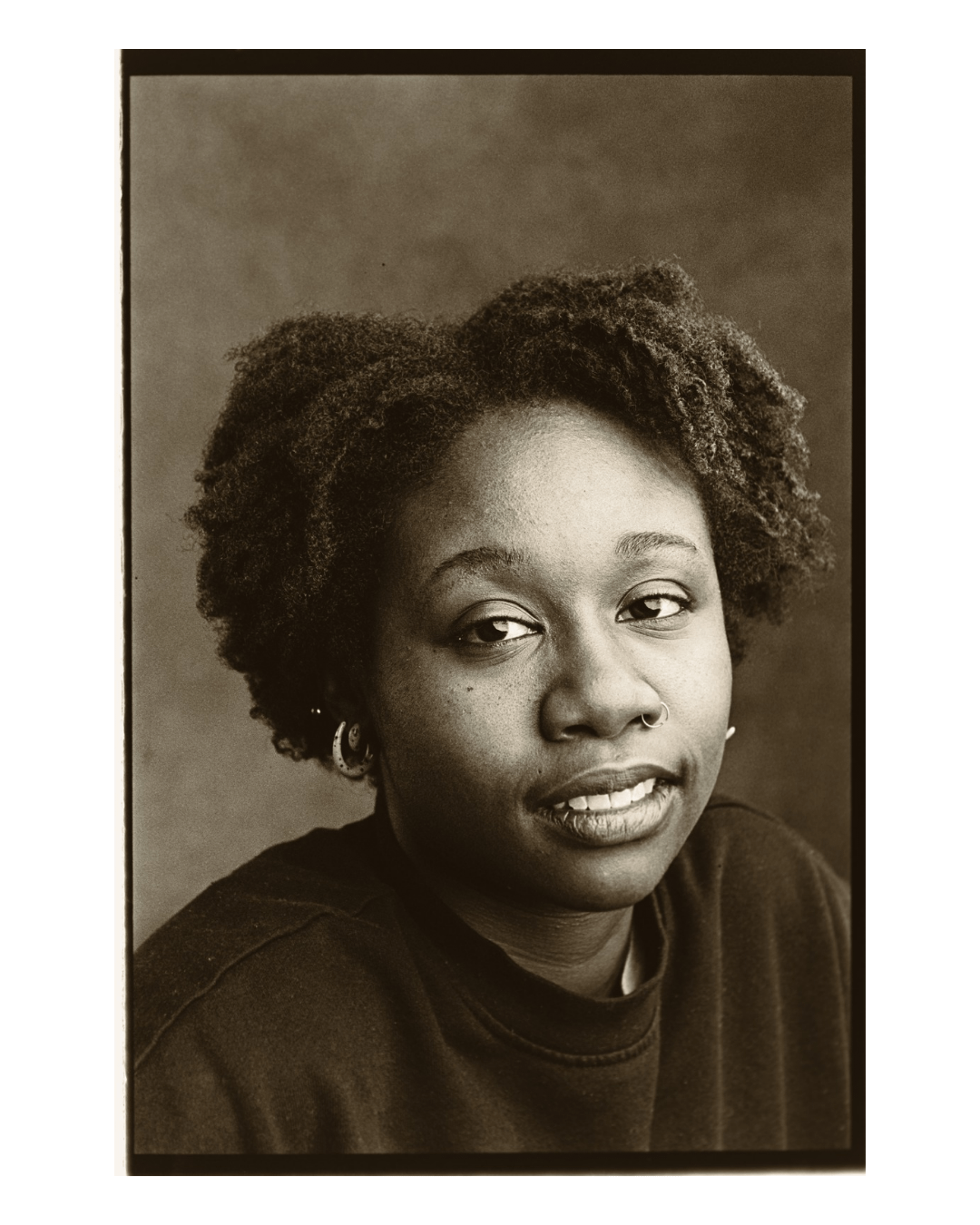A woman with curly hair and a nose ring looks towards the viewer.