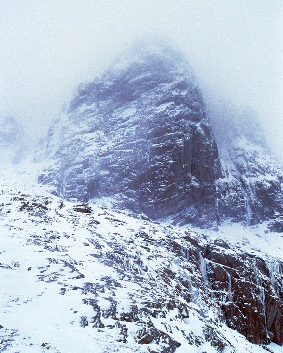 A snow-covered mountain rises into a hazy sky, with icicles hanging from rocks in the foreground.
